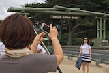 A woman poses for a photo under a sign that says "Great Ocean Road". In the foreground another woman takes her picture