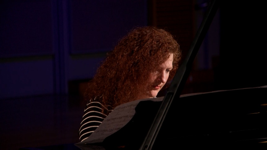 A woman playing a piano in a moodily-lit music studio.