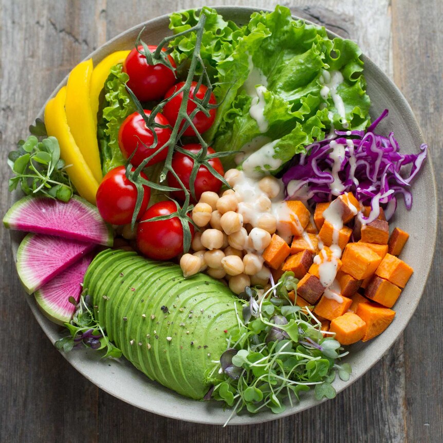 A bowl filled with fresh vegetables and fruits, including lettuce, capsicum, cherry tomatoes on the vine, and slices of avocado
