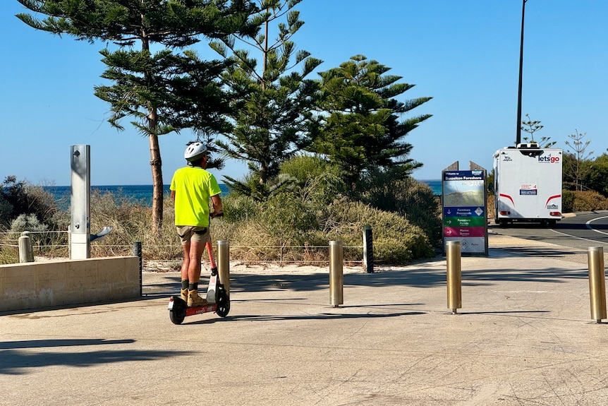 A man in a high-vis top rides an E-scooter along the foreshore in Busselton