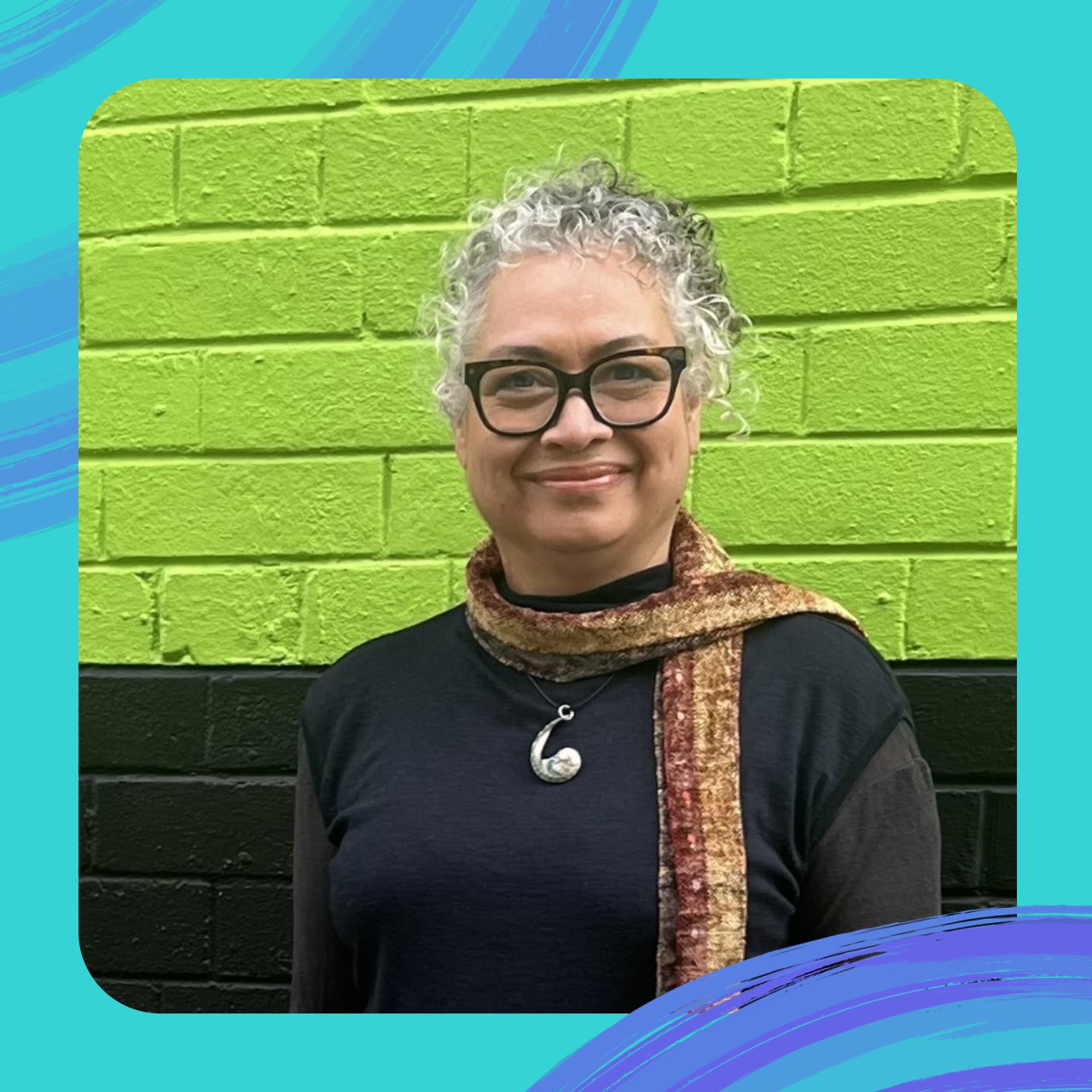 A portrait of Lynne Shori. She has curly grey hair and is wearing black eye classes and a brown scarf.