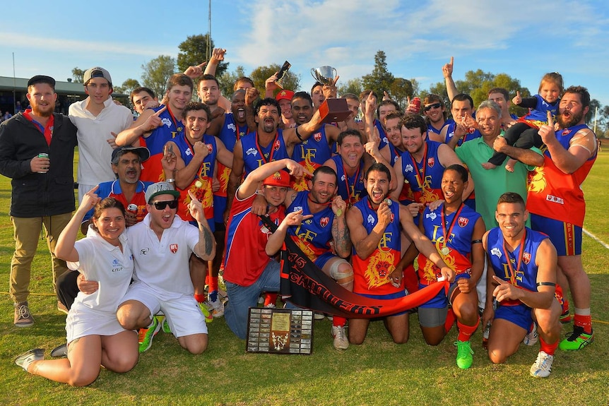 Football club celebrates a win wearing red and blue guernseys and holding trophies and medals