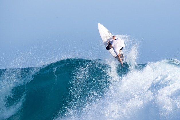 A surfer turns his board at the top of a big wave.