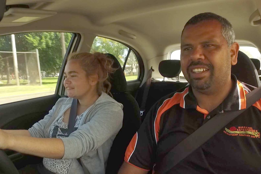 A driving instructor and a young girl sit in a car