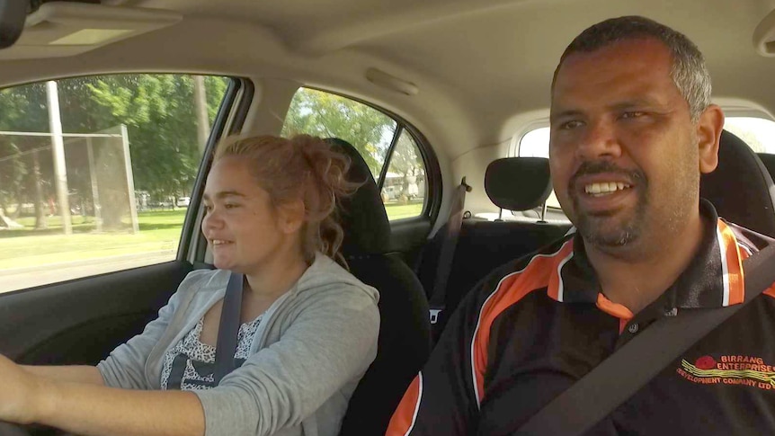 A driving instructor and a young girl sit in a car