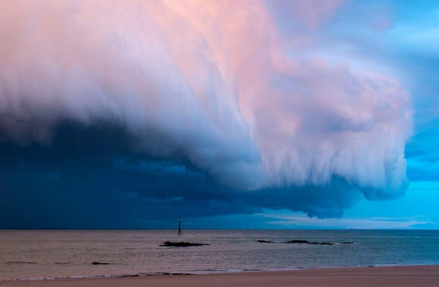 Large white and pink storm clouds roll in over the ocean towards the beach near Broome.
