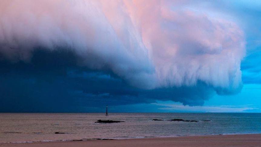 Large white and pink storm clouds roll in over the ocean towards the beach near Broome.