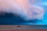 Large white and pink storm clouds roll in over the ocean towards the beach near Broome.