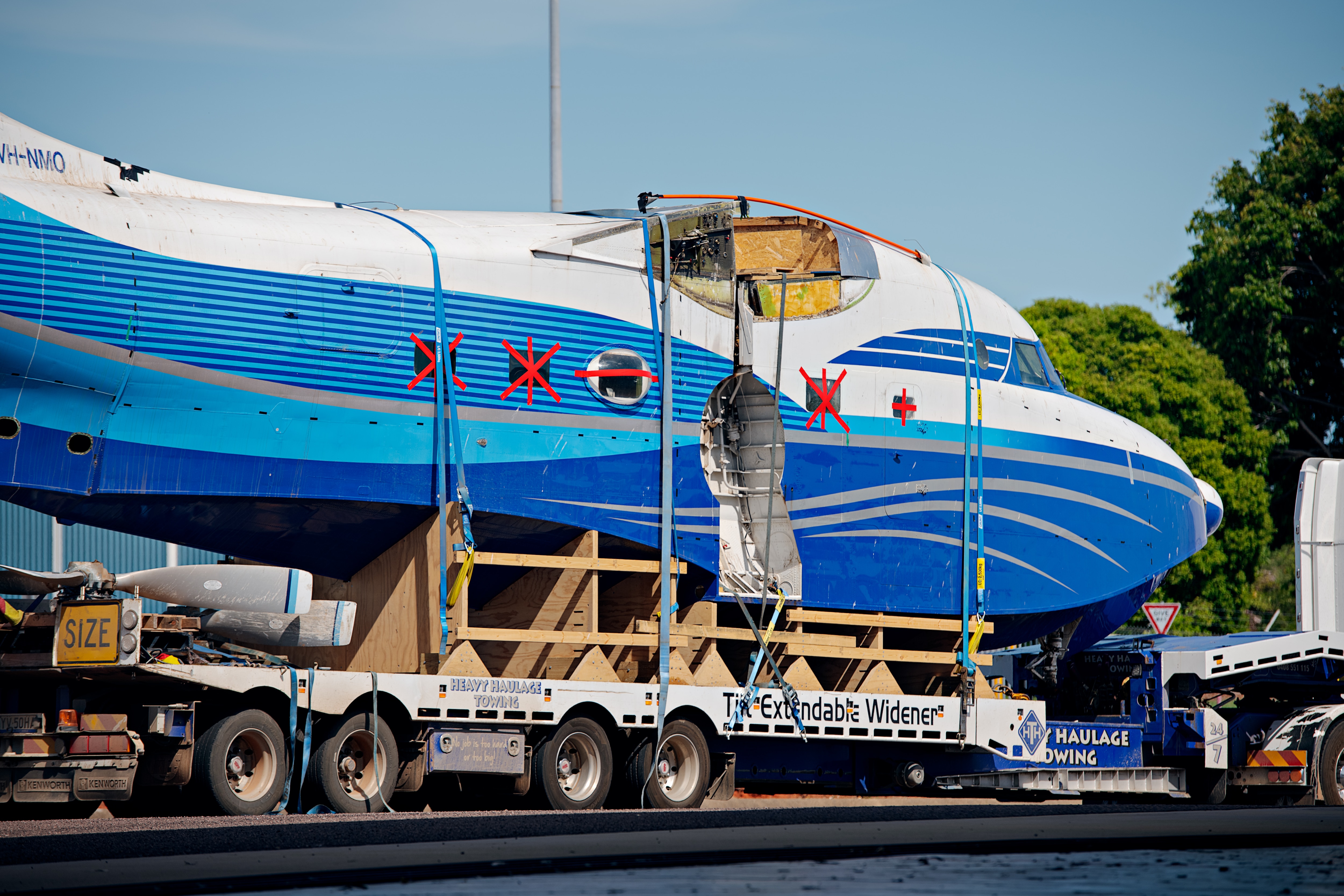 El exterior de un avión grande, azul y blanco, con cinta roja sobre las ventanas.