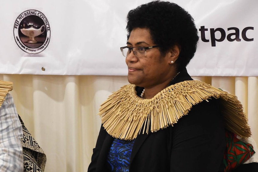 A fijian woman wearing a traditional necklace sitting in a room.