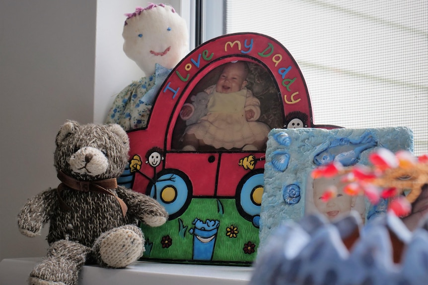 Red picture frame on window with picture of baby girl and brow teddy bear to the left. 