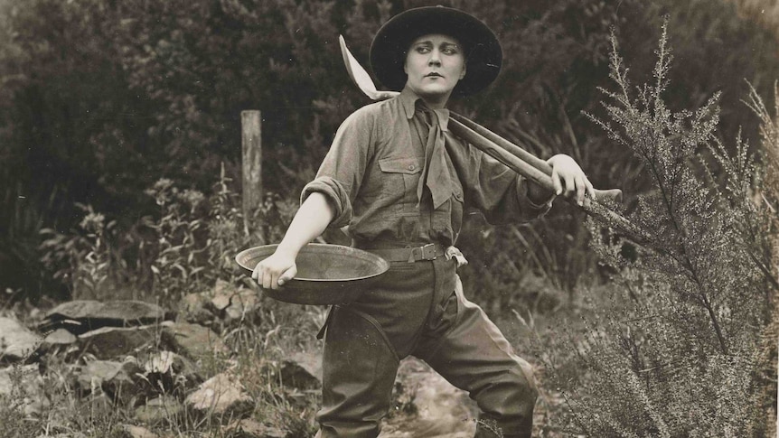 Black and white photo a woman in jodhpurs holding a pan and shovel