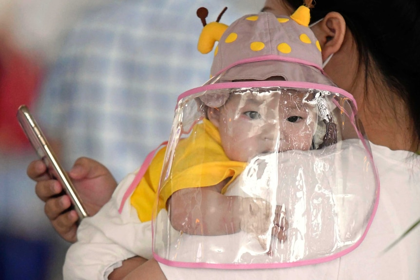 A baby with a face shield waits to board a plane at an airport in Wuhan.