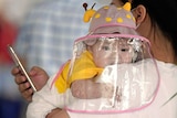 A baby with a face shield waits to board a plane at an airport in Wuhan.