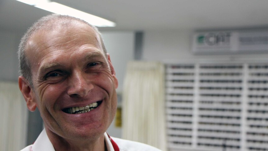 A man smiling at the camera in a room filled with bean samples