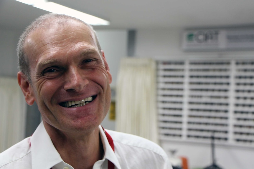 A man smiling at the camera in a room filled with bean samples