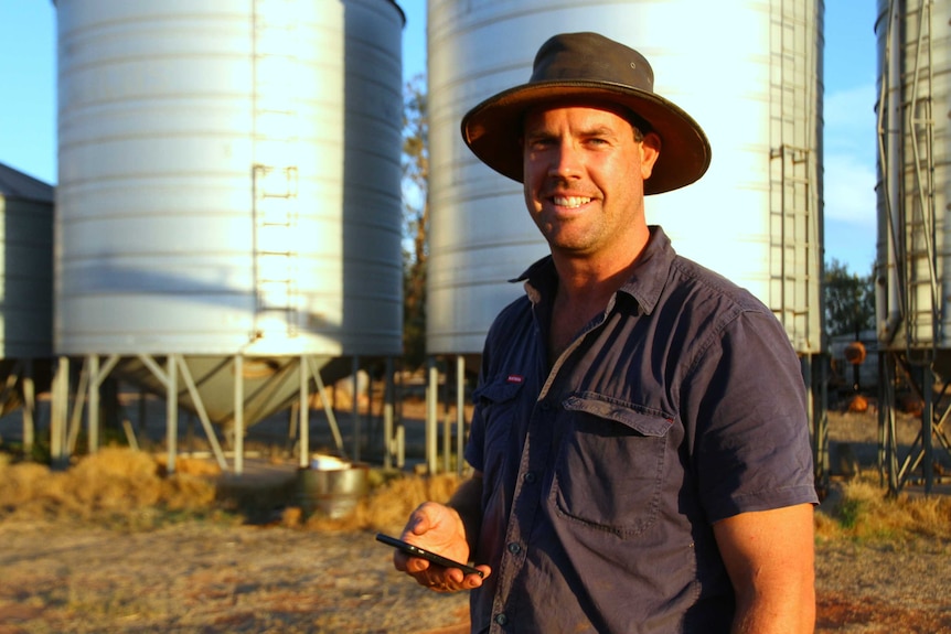 A man stands with a phone in his hand by a silo