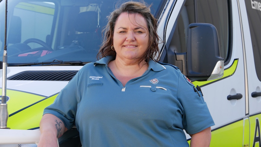 A woman stands in front of an ambulance and smiles