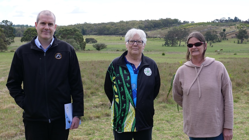 A man and two women standing in a field.