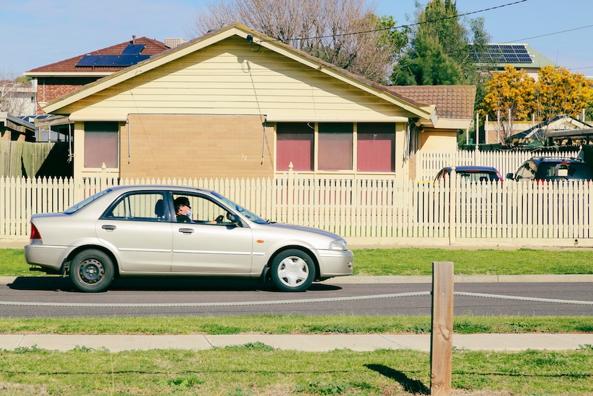 A man drives a sedan on a suburban street.