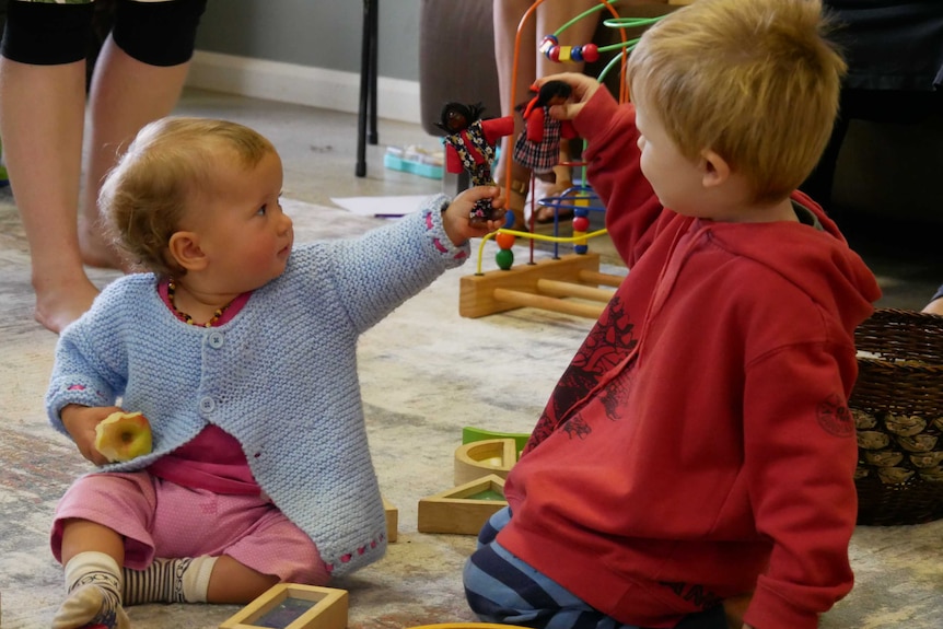 A baby girl and young boy play together on a mat.