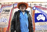 Colour photograph of artist Mumu Mike Williams standing in front of his artwork, painted onto old Australian Post mailbags