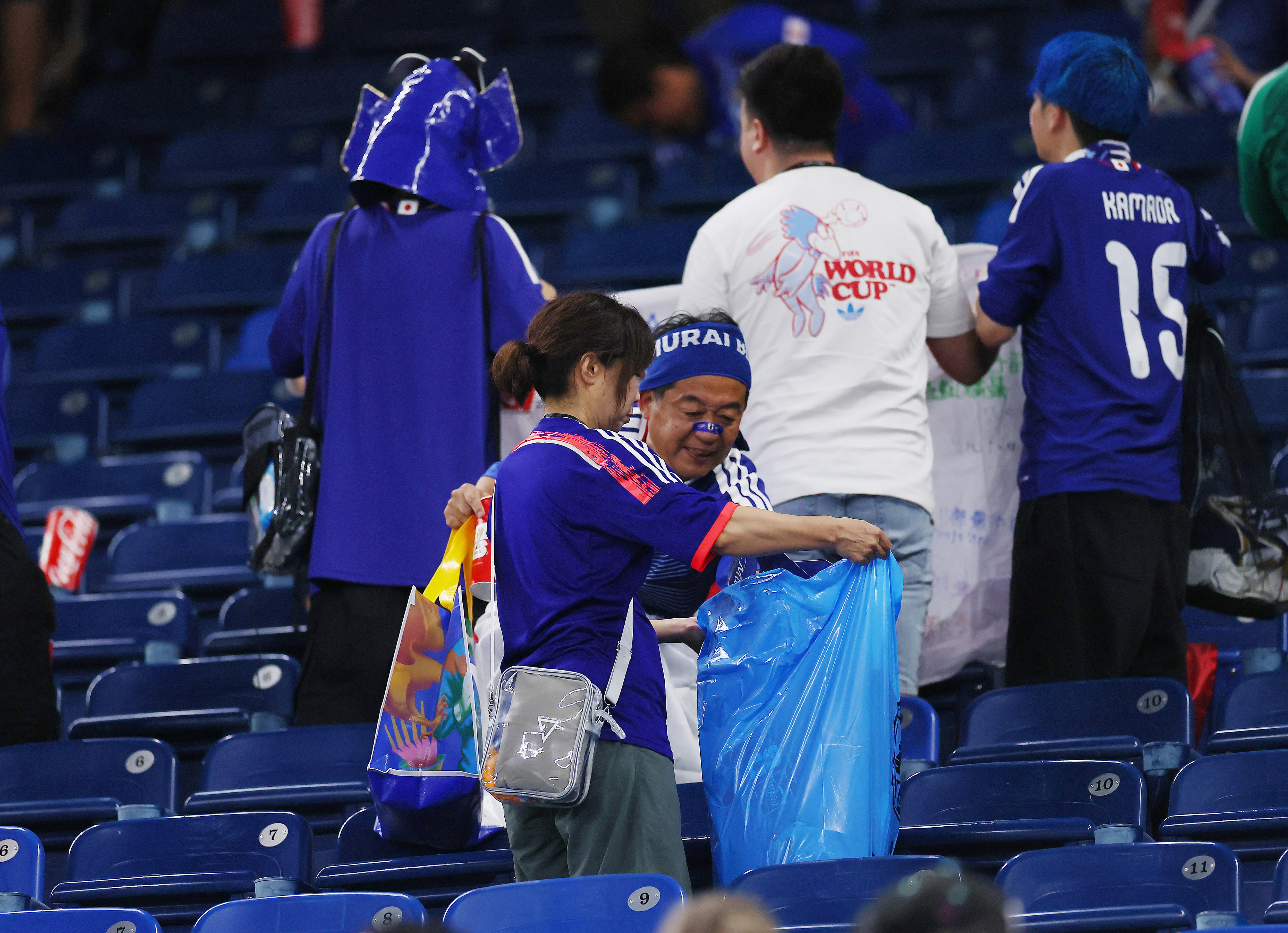 Two Japanese football fans dressed in blue clean up the stadium with a rubbish bag