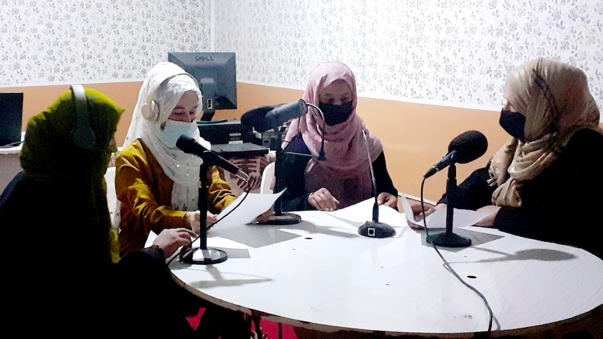 Four women sit at a table with micophones in front of them. 