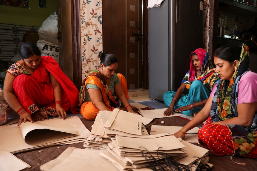 Four women sit in a circle and work with cardboard. 