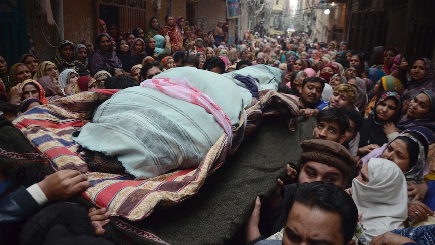 From a high vantage point you see down a crowded street with the body of a slain Pakistani shot carried in a blue wrap.