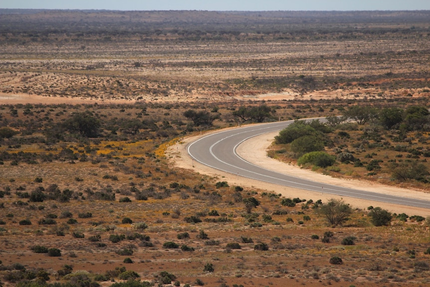 An outback highway snakes around a hill