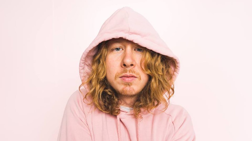 Ben Kweller wears a pink hoodie and stares at the camera.