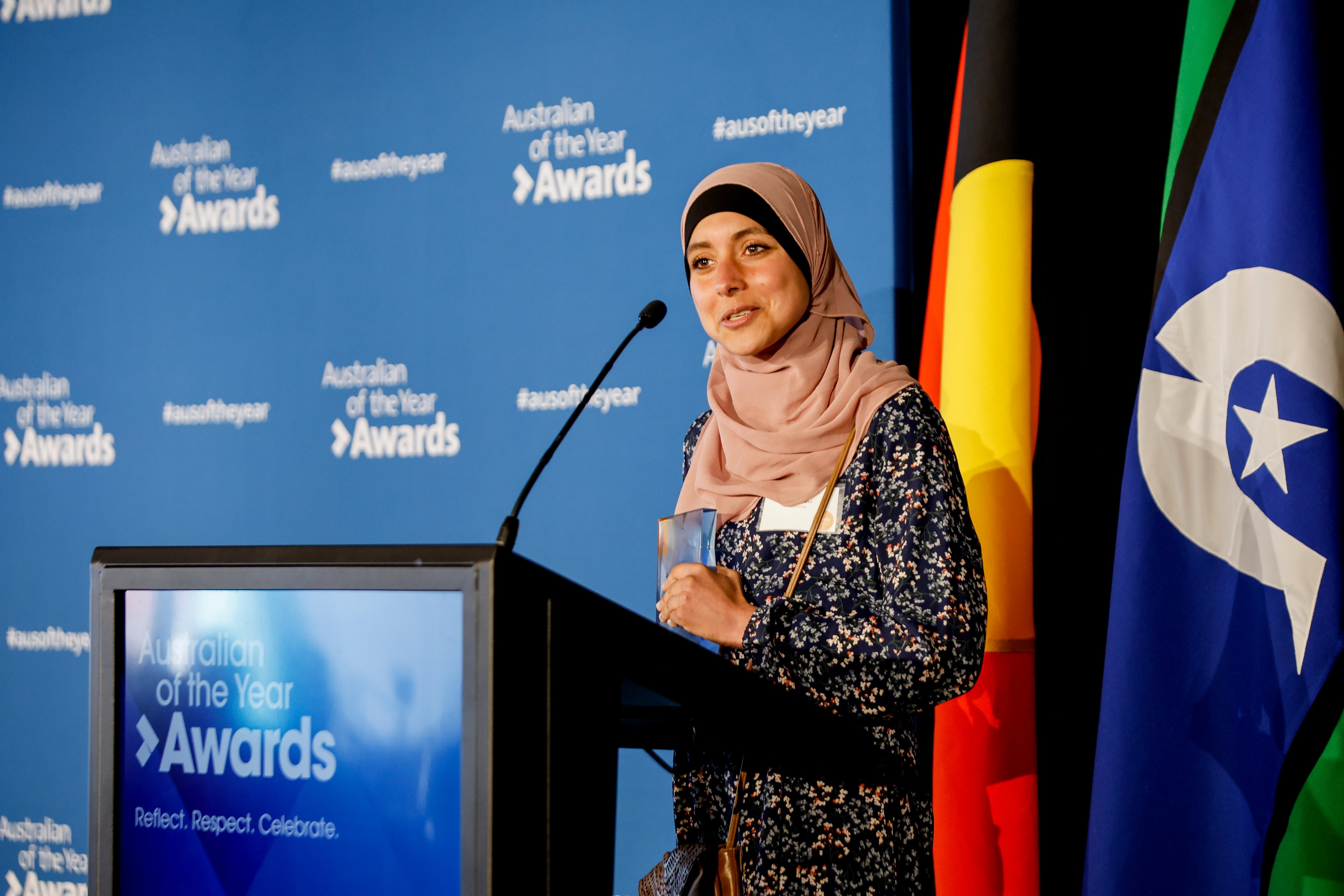 A young woman in a hijab talking at a lecturn