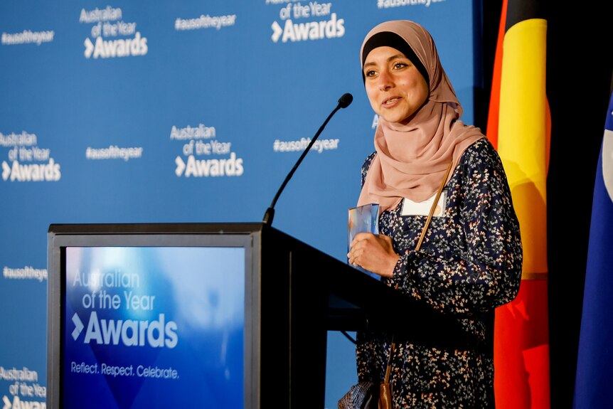 A young woman in a hijab talking at a  lecturn