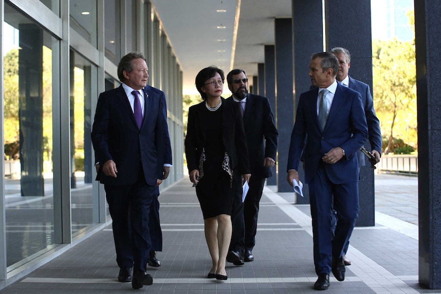 A group of business people and politicians dressed in corporate suits walk towards the camera outside a building.