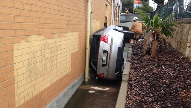 Image of car wedged between a shop and retaining wall
