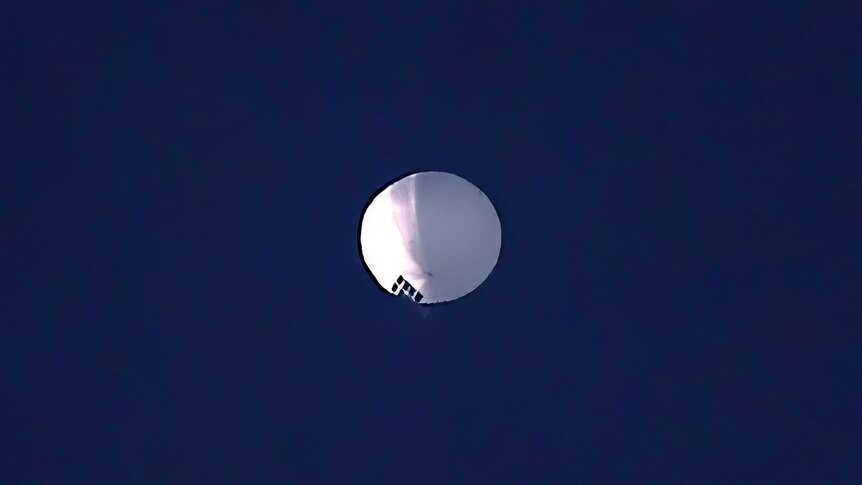 A high altitude balloon floats in a clear blue sky.