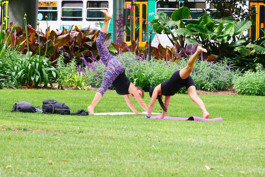 Two women do yoga in a park.