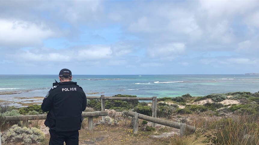 A police officer stands facing the beach at Port MacDonnell where it's believed a snorkeler was taken by a shark.