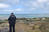 A police officer stands facing the beach at Port MacDonnell where it's believed a snorkeler was taken by a shark.