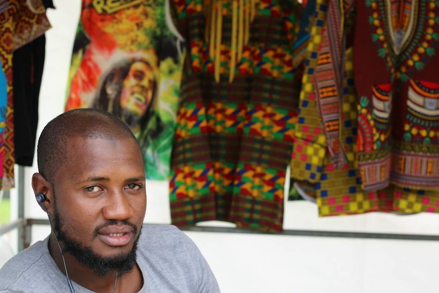 African-Australian man smiling at camera with Bob Marley print hanging behind him.