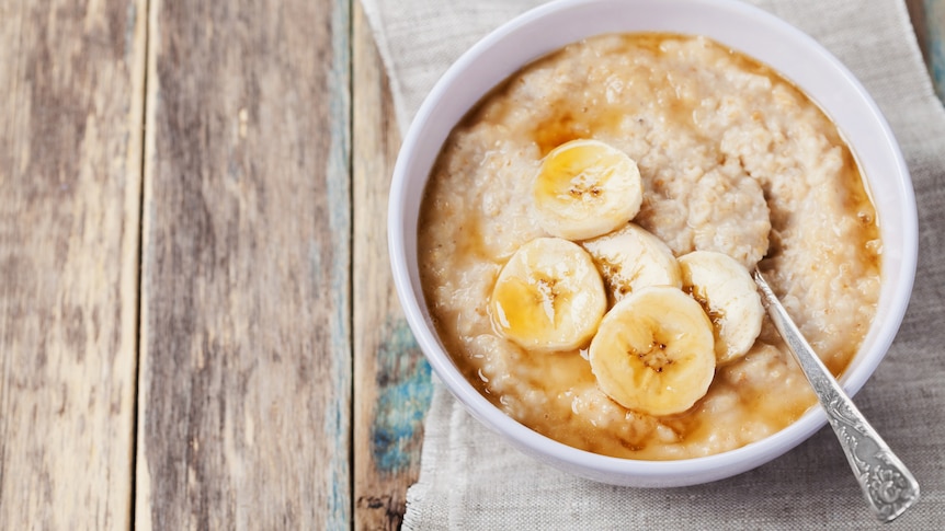 A bowl of porridge topped with banana and brown sugar sitting on a wooden table