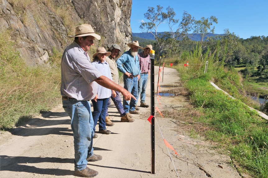 4 men and 1 woman standing on side of road pointing at cracks in a narrow mountain road