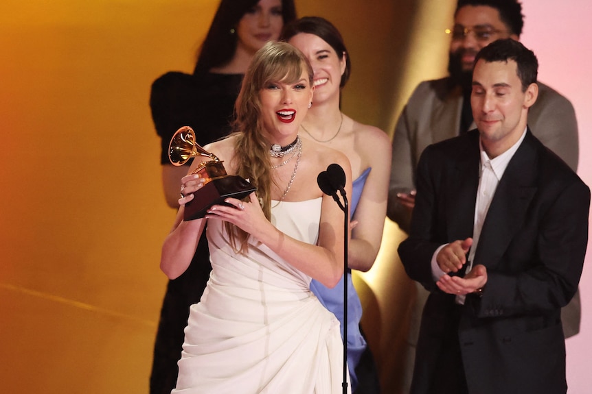 Taylor Swift smiles on stage while holding an award.