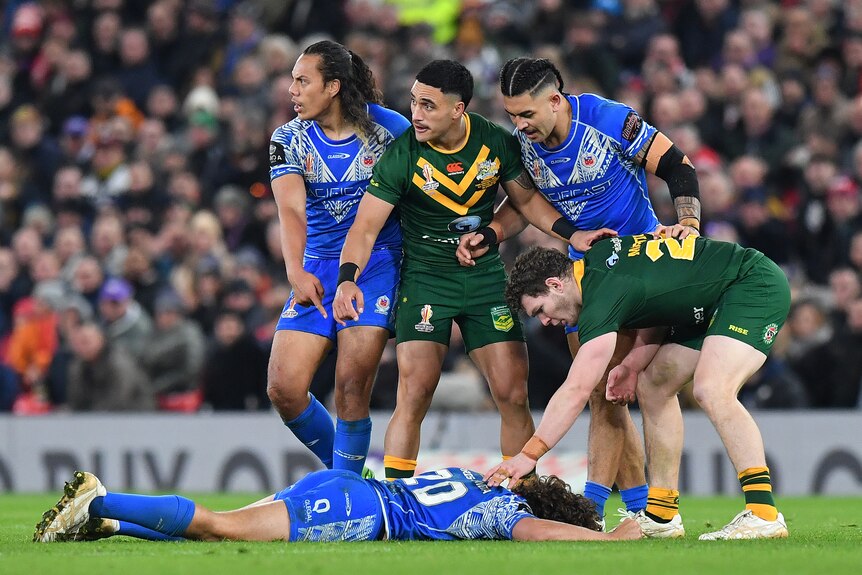 Samoan and Australian rugby league players gesture to officials to help a Samoan player lying knocked out on the ground.