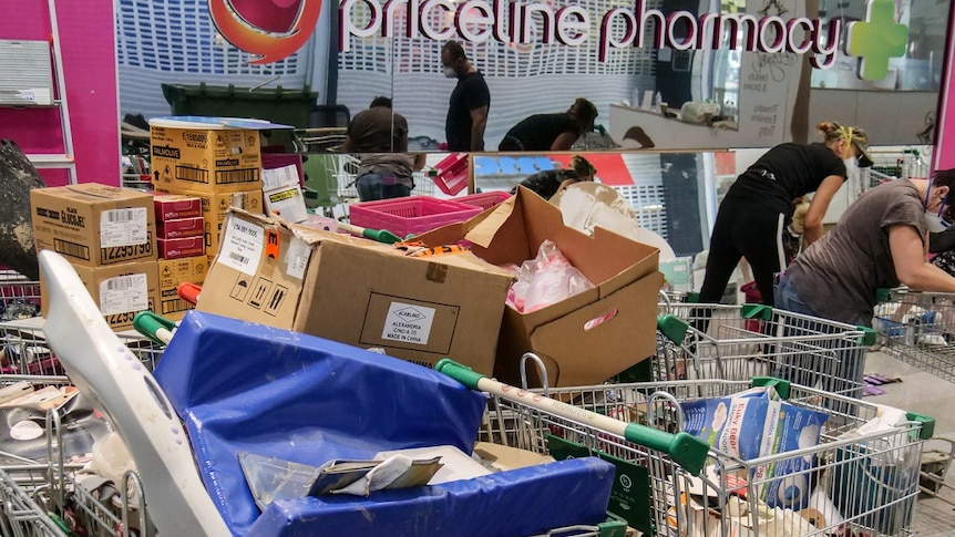 People, wearing face masks, clean up the Priceline pharmacy in Townsville after floods