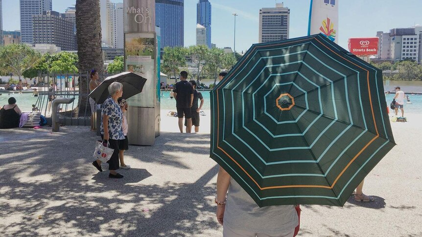 People shelter from the heat with umbrellas at South Bank in Brisbane on February 11, 2017 during a heatwave.