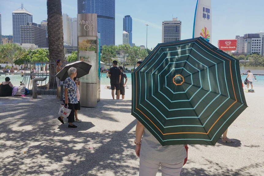 People shelter from the heat with umbrellas at South Bank in Brisbane on February 11, 2017 during a heatwave.