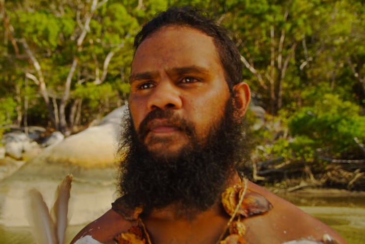 An Aboriginal man looks ahead with mangroves behind him.