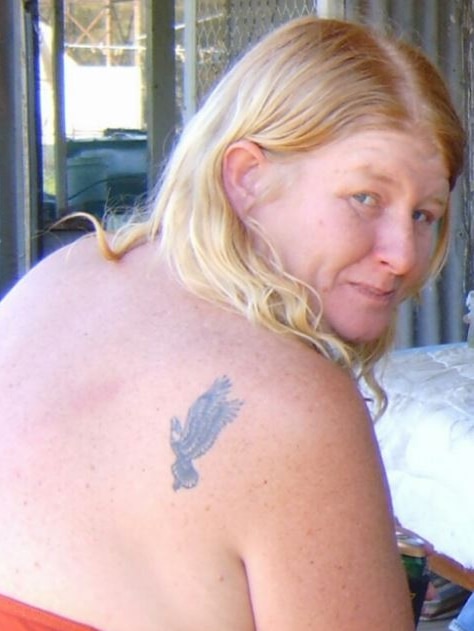 A woman with a tattoo on her shoulder blade looks back towards the camera.